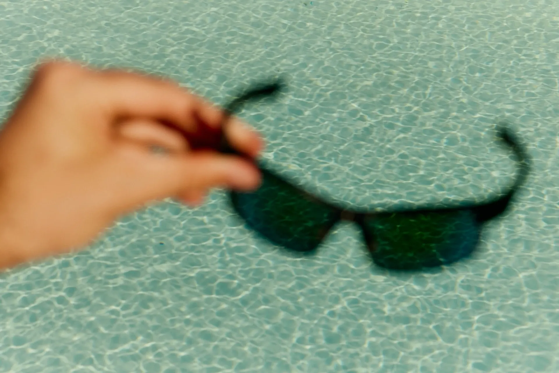Someone holding a pair of sunglasses in front of a swimming pool